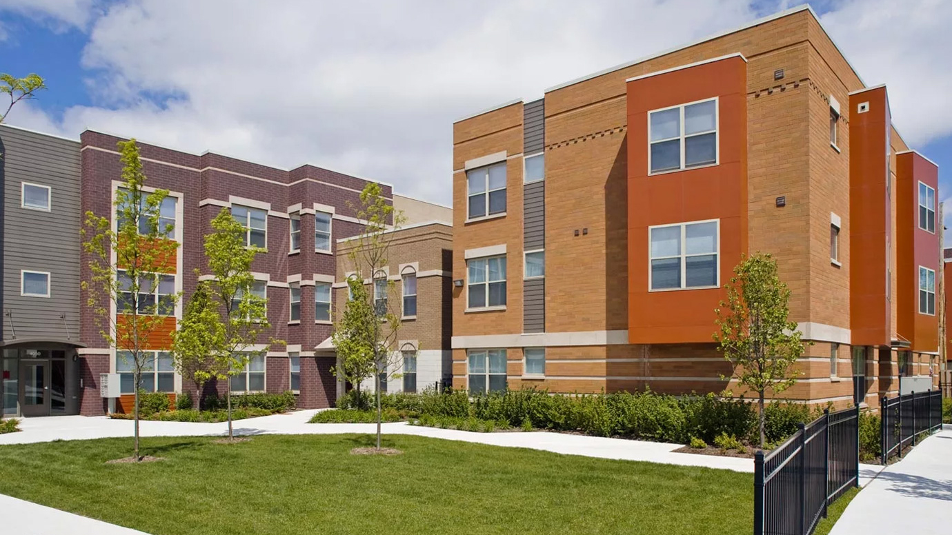 A three story housing complex with a landscaped lawn.